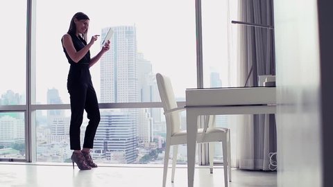 Successful businesswoman with tablet computer standing by window, slow motion.