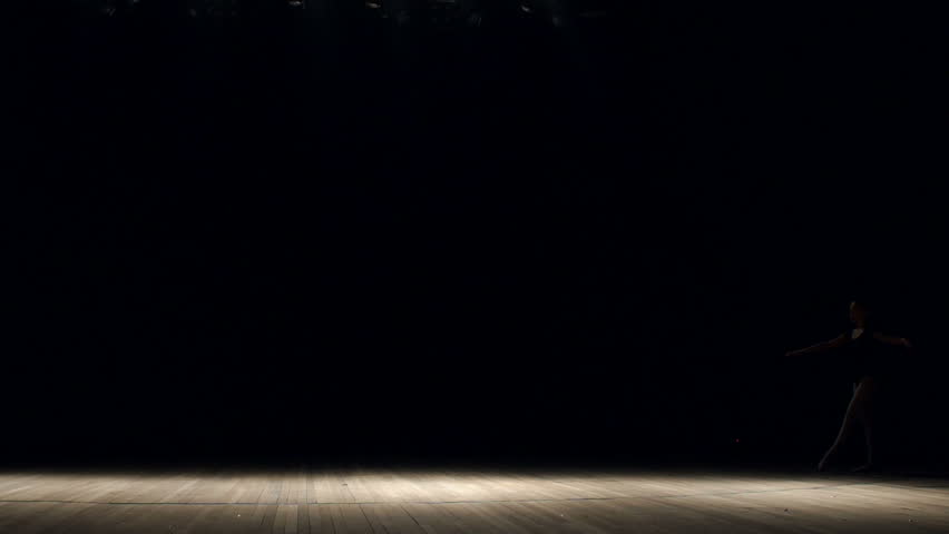 Girl ballerina doing horizontal twine in the air on stage on black background, slow motion. Girl doing gymnastic flip. Acrobatic flip. Ballet. Dancer.