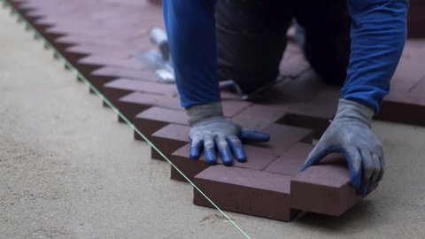 Using the butt of his trowel, a hardscaper taps the red brick pavers into place on a bed of sand.