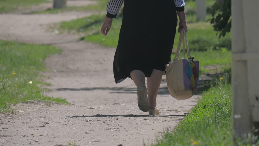 fat woman is walking outdoors track path around grass the summer with bag provincial town city