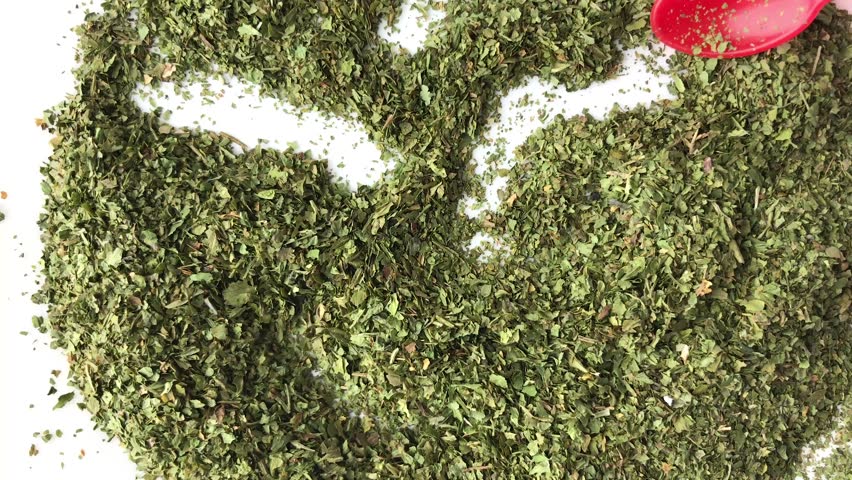 A very close view of cilantro flakes being stirred with a red plastic spoon on a white plate.