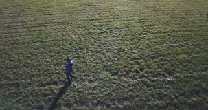 Aerial orbit of a lone guitar player rocking out and wearing hat, jean jacket, jeans in a large open grass field.