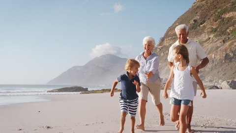 Grandparents Chasing Grandchildren Along Beach On Summer Vacation