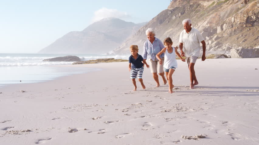Grandparents Chasing Grandchildren Along Beach On Summer Vacation | Shutterstock HD Video #1011609704