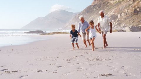 Grandparents Chasing Grandchildren Along Beach On Summer Vacation