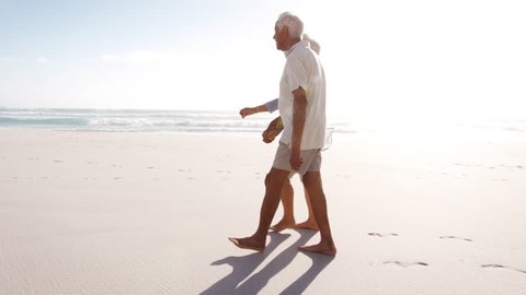 Romantic Senior Couple On Summer Vacation Walking Along Beach