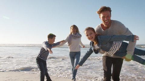 Family On Winter Beach Running Away From Advancing Waves