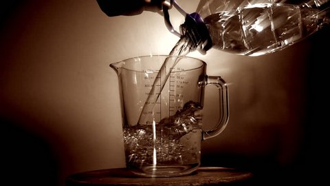Slow motion shot of a man’s hands holding a large plastic bottle and pouring water into a glass measuring jug.