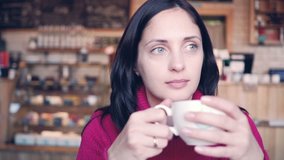 A young woman sits at a table in a cafe and drink coffee. Slow Motion footage