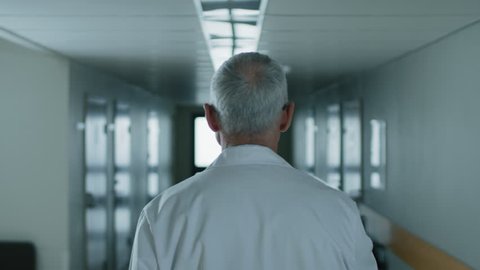 Following Shot of the Professional Male Doctor Walking Through Hospital Hallway. Portrait Footage. Shot on RED EPIC-W 8K Helium Cinema Camera.