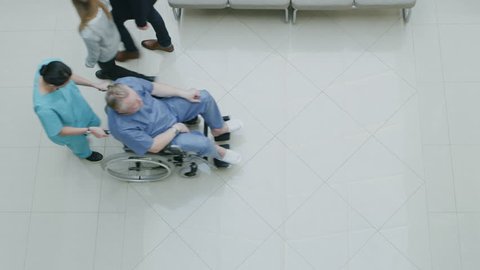 High Angle Shot In the Hospital Lobby of Medical Personnel Pushing Patients in Wheelchairs, Doctors and Patients Working and Walking. New, Clean Hospital. Shot on RED EPIC-W 8K Helium Cinema Camera.