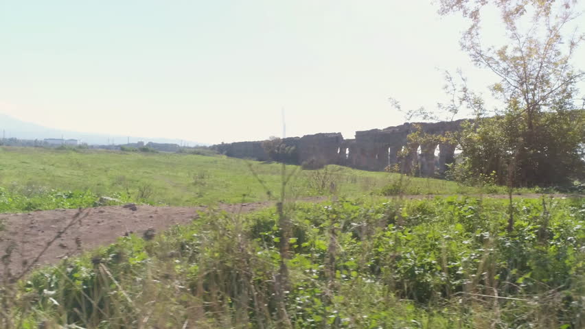 Young man cyclist on dirt road along ancient roman aqueduct in orange sportswear aerial view drone