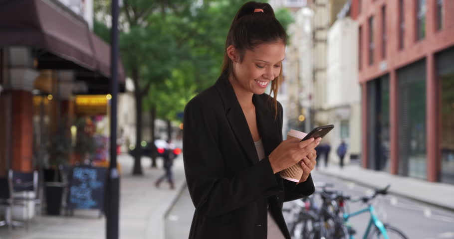 Young Caucasian business woman text messaging outside cafe on mobile phone while downtown. Happy Millennial Professional female texting with smartphone in the city by coffee shop. 4k | Shutterstock HD Video #1011645164