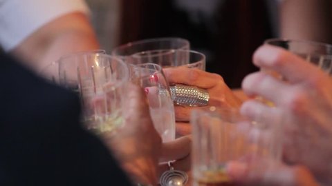 People with glasses of alcohol and glasses of whiskey celebrate at the table. Hands of people with glasses of whiskey close-up. Shallow depth of field