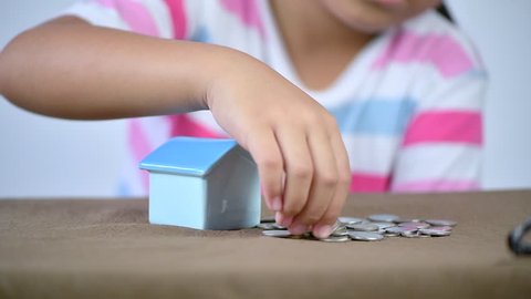 little hand putting coin in house piggy bank, saving money for buy new house concept