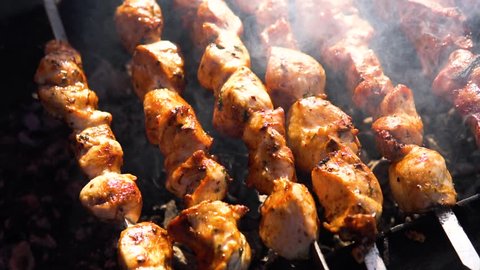 Appetizing delicious fried pieces of meat on skewers are roasted on a large grill in the open air. The chef prepares a barbecue. slow motion
