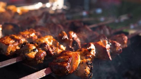Appetizing delicious fried pieces of meat on skewers are roasted on a large grill in the open air. The chef prepares a barbecue. slow motion