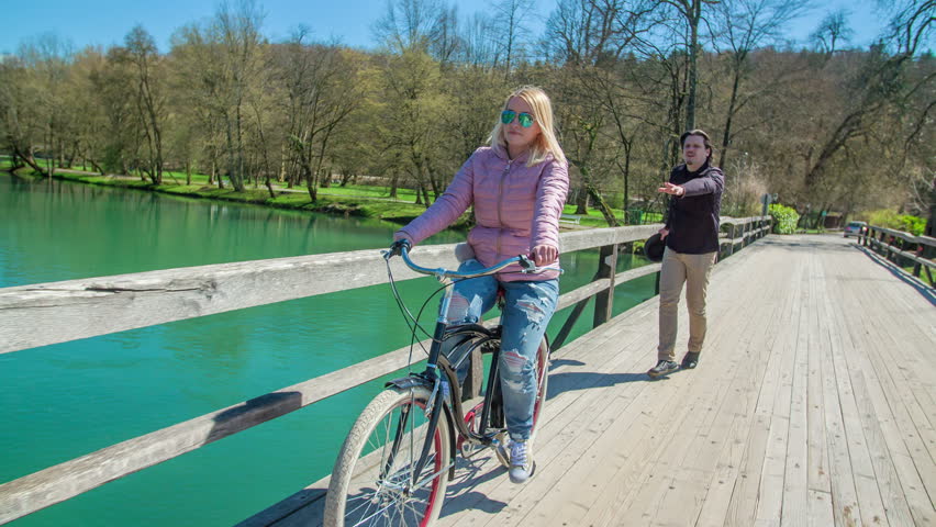 A young woman is riding her bicycle and a man is running after her and tries to catch her.
