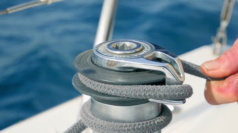 Sailor mans hand winding up grey rope arround sailing boats side winch. Closeup on sailor securing rope. Filmed on sailing tip in Adriatic sea in slow motion hd.