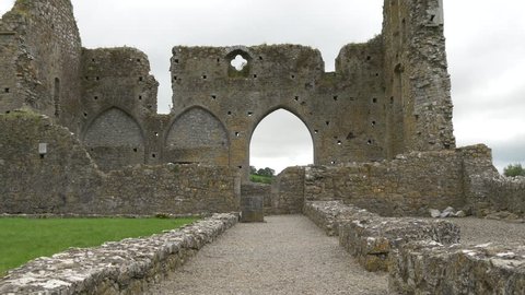 Cashel, Ireland - May, 2016: Zoom out view of stone wall ruins, arched gate and clover shape window at Hore Abbey