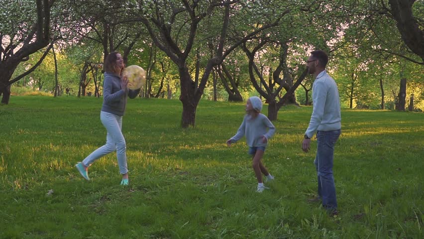 parents and two daughters play sport with ball in spring park in the blooming garden. Active leisure.