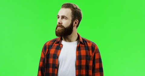 Portrait of the handsome caucasian man with a beard and in the red plaid shirt turning to the camera and crossing his hands while smiling. Green screen. Chroma key.