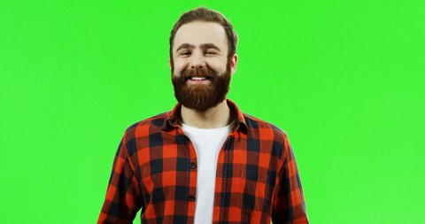 Handsome Caucasian man with a beard standing in front of the camera and smiling with a provocative face on the chroma key background. Green screen.