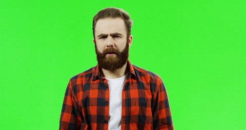 Portrait of the good looking Caucasian man with a beard standing in front of the camera and doing knock knock gesture, then waving his hand on the green screen background. Chroma key.