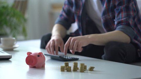 Man calculating money, putting coins into piggy bank, family budget planning