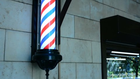 Barber pole rotating on wall in hairdresser shop. Barber pole spinning at barbershop. Vintage barbershop and hairdresser symbol. Traditional barber pole rotating in barbershop