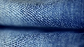 Suggestive dolly shot super macro of details of a pair of denim jeans pants. Closeup of youthful texile material of jeans trousers. Focus on two folds of denim pants laid in a clothing store.