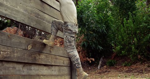Side view of Caucasian military soldier climbing a wooden wall at boot camp during obstacle course