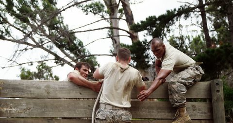 Male soldiers assisting their team mate to climb a wooden wall at boot camp 4k