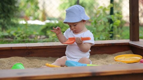 Little baby boy, playing in a sandpit with toys outdoors
