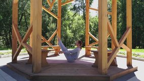 Caucasian woman practicing yoga in the park pavilion. Finish of the set which focuses on abdominal and back muscles training. Sunny spring day. Camera stands still