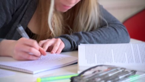A medium tilt shot of a female student making notes from a textbook as she studies.