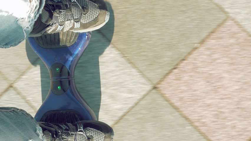 Man is riding hoverboard or electric self balancing gyro scooter board on the side walk. Modern and trendy urban transportation gadget. POV first person view. Vertical format video.