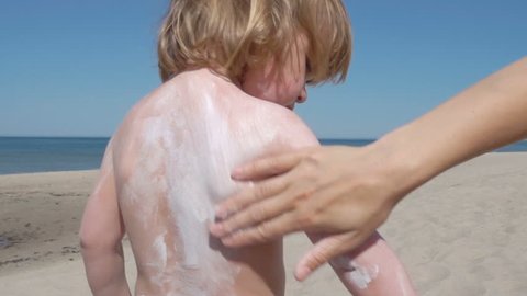 Mother applying sunscreen lotion on son back at beach. Mother preparing child for bath in sea. 