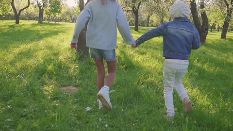 Children run through the park with Blossoming orchard. steadicam shooting of two girls who run through the park and smile. Slow motion