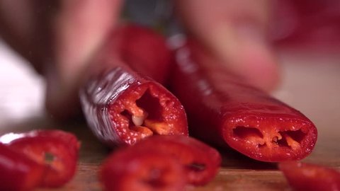 Knife cutting red chilli pepper on wood
