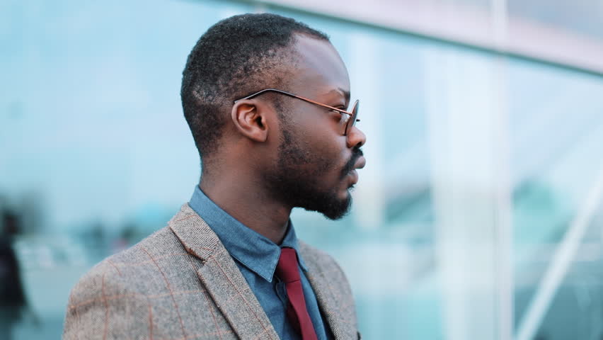 African American businessman in sunglasses stands thoughtful on the street near business center