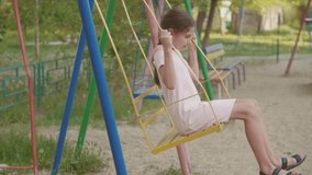 little girl swinging on an old swing slow-motion video. schoolgirl playing on the street swinging on the swing childhood outdoors. girl and swing lifestyle concept
