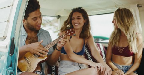 Group of friends laughing and playing music in vintage surf van, beach lifestyle