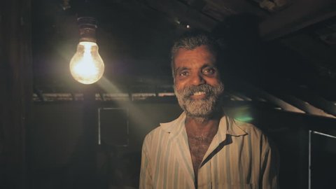 A poor man smiles after a tungsten light bulb slowly turning on or brighten up in old rural house. A happy farmer smiling after a light bulb turn on and receiving electricity for the first time. 