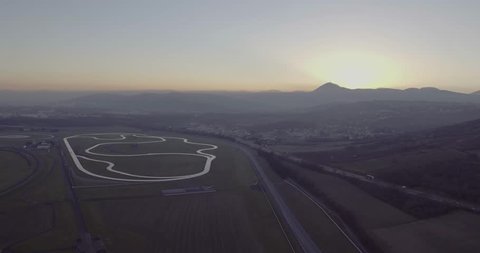 Aerial shot / Drone shot of a French test track, sunset in the back ground of the landscape, race track in the middle of the frame and drone pans to the right