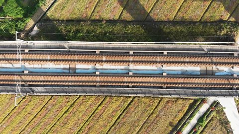 Looking down at Chinese high speed train tracks on raised platform. Drone shot of moving gaotie on elevated railway.