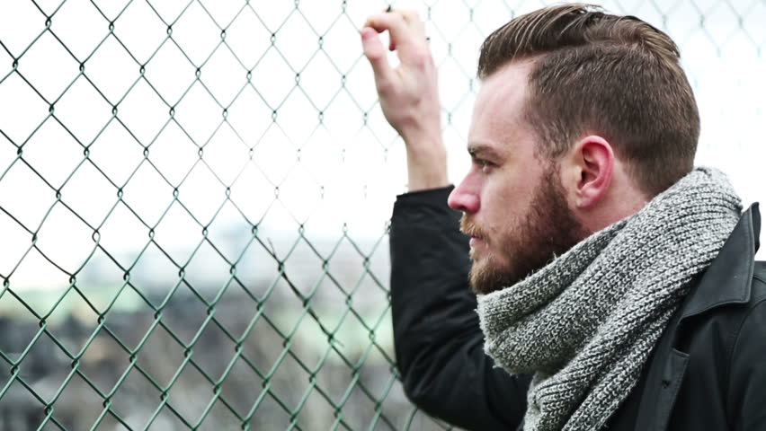 Focused and confused man leaning outside wearing a jacket and scarf. A dull and cloudy sky.