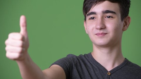 Young handsome Iranian teenage boy against green background