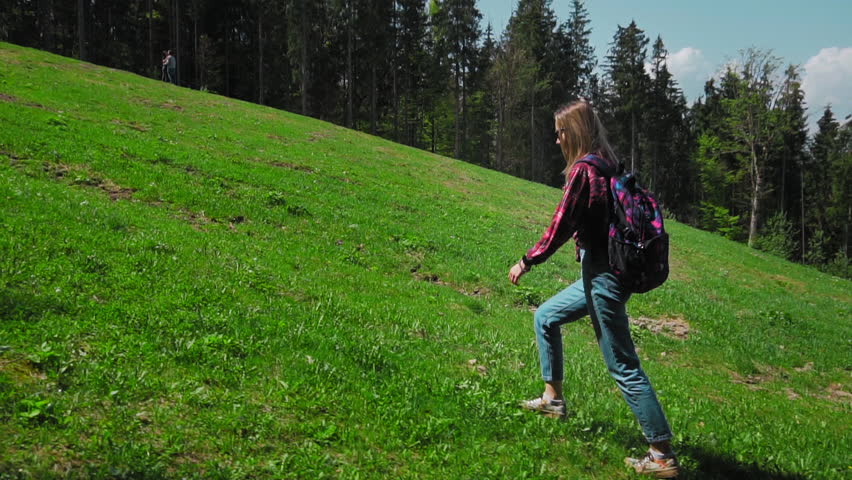 A young caucasian woman with a backpack and sunglasses rises up the mountain. The concept of personal growth, overcoming difficulties in business, motivation of the individual, freedom and self