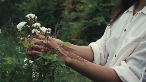 Close up shot of woman touching and enjoying wild flowers in a forest. Woman with exotic white flowers outdoor in nature. Henna art.